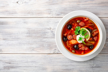 Traditional Russian meat soup Solyanka in bowl on rustic wooden table. Top view. Copy space.