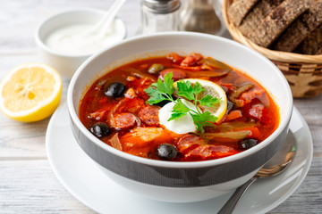 Traditional Russian meat soup Solyanka in bowl on rustic wooden table. Selective focus.
