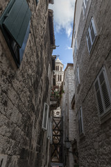 an ancient European city in Croatia, a narrow street in the old town; on both sides of the street are stone-built houses, all windows have wooden shutters; view from the bottom up