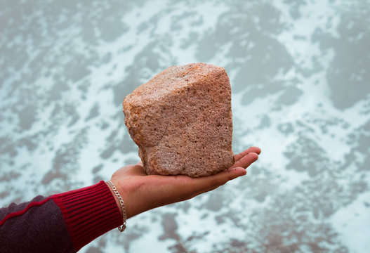 mano sosteniendo una roca, piedra de color rosa anaranjado con textura y calidad de fondo de pantalla, fondo nevado y rocoso