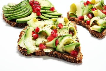sliced avocado and ripe pomegranates on toast bread with spices and avocado.