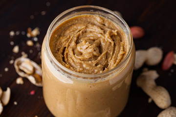 Homemade peanut butter in a glass jar on a wooden background with shells and nuts. Food stylish horizontal shot
