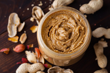 Homemade peanut butter in a glass jar on a wooden background with shells and nuts. Food stylish horizontal shot