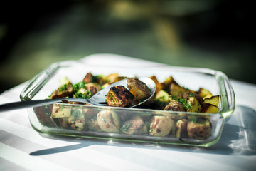 Pyrex Platter full of roasted potatoes. Close up shot taken outside on a white tablecloth. Blurry forest in the background