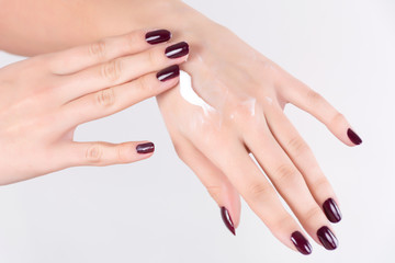 Young girl applying hand cream on skin and girl has red wine nails polish gel, isolated on white background. Female beauty, manicure and cosmetics concept. Close up, selective focus.