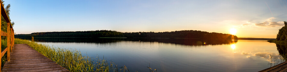 ein Panorama von einem See umgeben von Wald bei Sonnenuntergang - obrazy, fototapety, plakaty