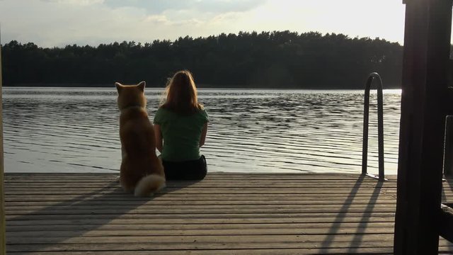 eine Frau sitzt mit ihrem Hund (Akita Inu) am See