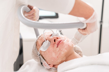 Naklejka premium Anti acne phototherapy with professional equipment. Beautiful woman in beauty salon during photo rejuvenation procedure. Laser face skin treatment at cosmetic clinic. Hardware cosmetology