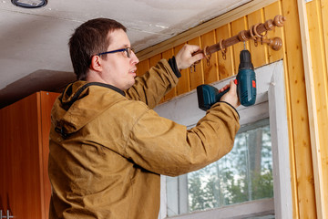 A man collects cornice. The screw is screwed with a screwdriver. Repair in the house in the country