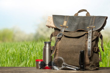 Vintage backpack, compass, sunglasses and binoculars, map, thermoses for tea. Tourism, travel, adventure on the natural background of summer, breath and warmth. Banner