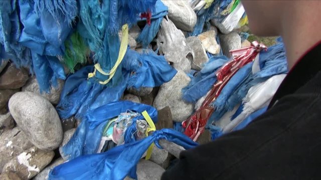 Boy ties blue ribbon on shaman obo sacrifices on stones in Mongolia.