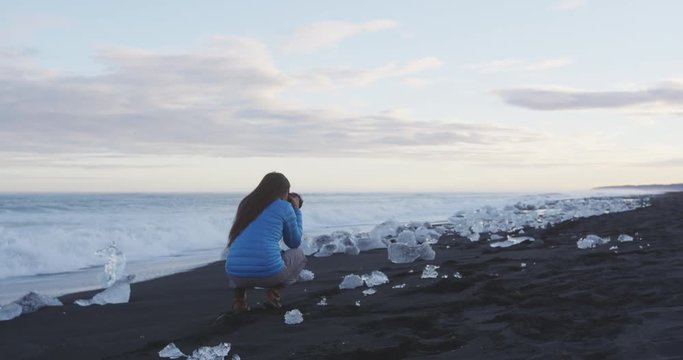 Photographer taking photos in nature on Iceland Diamond Beach with Ice. Woman photographing at okulsarlon Iceberg beach aka Breidamerkursandur on South coast of Iceland. RED EPIC SLOW MOTION