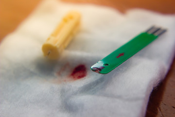 close up of diabetes test strip and needle laid with blood drop on cotton