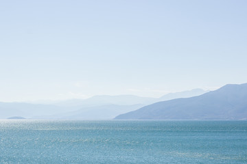 Obraz premium abstract picturesque scenic landscape of big lake natural reservoir foreground and mountain silhouettes in fog with sky background in sun rise morning time 