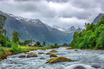 A bird view over a river with strong current flow among a forest and big mountains in the background in Norway