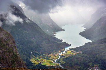 Naklejka na ściany i meble An aerial view of the fjords, heavy clouds around and a small village with houses on the edge of it in Norway