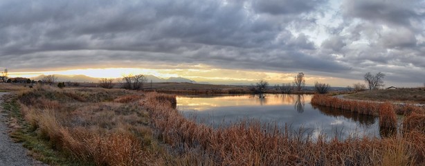 Views of Josh’s Pond walking path, Reflecting Sunset in Broomfield Colorado surrounded by Cattails, plains and Rocky mountain landscape during sunset. United States.
