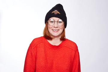 Human facial expressions, emotions and feelings. Portrait of funny funky teenage hipster lady wearing stylish knitted hat and sweater, having happy look, laughing at camera, posing at blank white wall