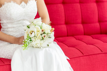 Bride in wedding suite with bouquet flower in her hands sitting on chair