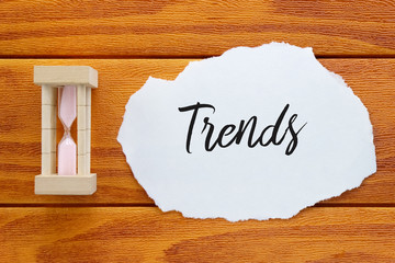 Top view of sand clock and piece of paper written with Trends on wooden background.