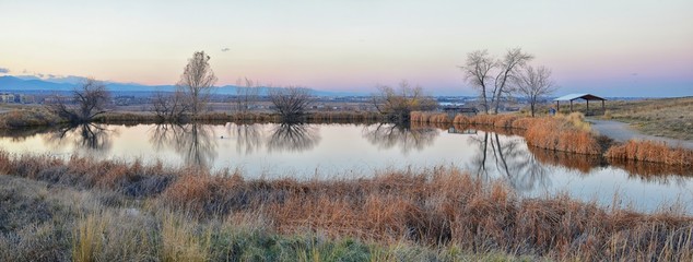 Fototapeta premium Views of Josh’s Pond walking path, Reflecting Sunset in Broomfield Colorado surrounded by Cattails, plains and Rocky mountain landscape during sunset. United States.