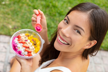 Acai bowl healthy eating Asian woman showing fruits smoothie breakfast outside in park for lunch. Diet vegan food closeup. Dragonfruit puree, bananas, strawberries, mangos, coconut, flax seeds.