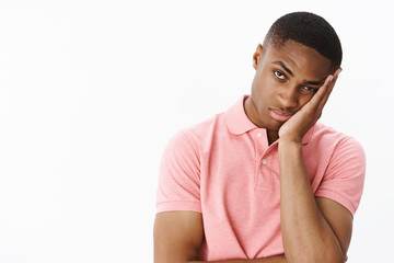 How long it lasts. Bored and indifferent displeased young african american male student leaning face on palm looking at camera with boredom and apathy feeling tired posing over gray background - Powered by Adobe