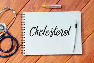 Top view of stethoscope,syringe,pen and notebook written with Cholesterol on wooden background,...