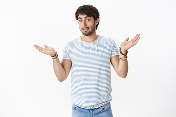 Fototapeta premium Oops sorry. Awkward and intense young attractive male with bristle and blue eyes smiling guilty as shrugging with hands spread sideways making mistake, apologizing being clueless how it happened