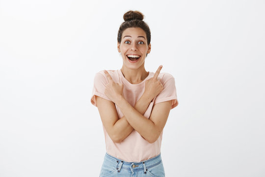 Portrait of delighted and impressed good-looking surprised woman pointing sideways as crossing arms on chest, showing right and left corner and reacting amused on great products on sale, smiling