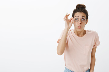 Girl putting on glasses realising how world look without blur folding lips bending towards camera amused and impressed standing excited and speechless with astonished expression over gray background