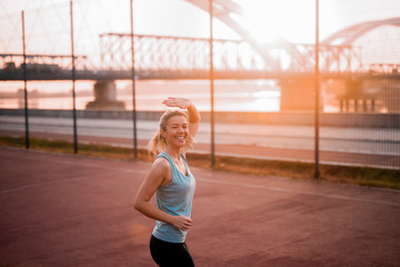 Smiling young fit girl on early morning jogging waving at her friend.