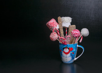 Blue Christmas mug with a snowman filled with candy pops, marshmellows and candy canes on a black background with text space.  Christmas baked gifts.
