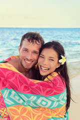 Fototapeta na wymiar Swimming romantic couple wrapped in bathing towel on beach. Portrait of happy young interracial couple embracing each other having fun during holidays vacation travel. Asian woman, Caucasian man.