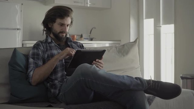 Relaxed young man using tablet while sitting on sofa at kitchen.