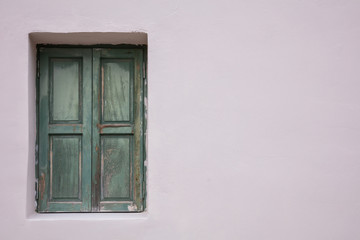 Old fashioned worn window with green wooden shutters, closed, on painted wall background.