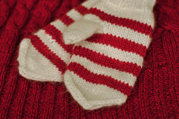 Knit. Homemade knitted striped mittens on knitted pattern background. Red color.