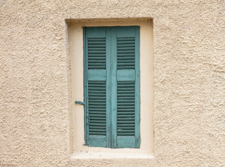 Old fashioned worn window with green wooden shutters, closed, on plastered wall background.