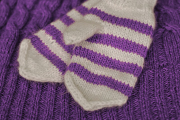 Knit. Homemade knitted striped mittens on knitted pattern background. Purple color.
