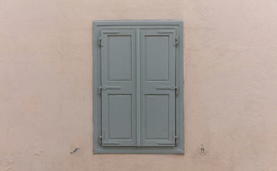 Fototapeta na wymiar Wooden window with grey shutters, closed, on painted wall background.