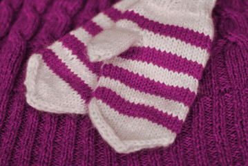 Knit. Homemade knitted striped mittens on knitted pattern background. Purple color.