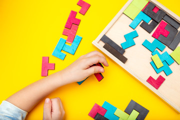 Wooden puzzle and kids hands on yellow background. Flat lay