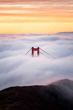 Golden Gate Bridge tower above the blanket of fog with brilliant sunrise colors