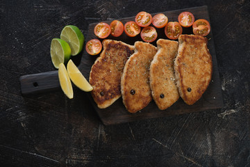 Obraz na płótnie Canvas Black wooden serving board with fried fish cutlets made of pike fillet, flatlay over dark brown stone background with space