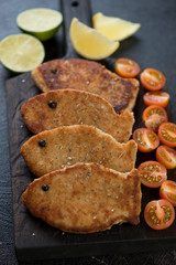 Close-up of roasted fish cutlets with cherry tomatoes, lemon and lime, selective focus, vertical shot