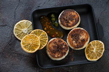 Cast-iron serving pan with curd pancakes or syrniki on a cracked asphalt background, studio shot