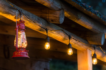 Red metal storm lantern hung outside rustic log cabin. © illuminaphotographic