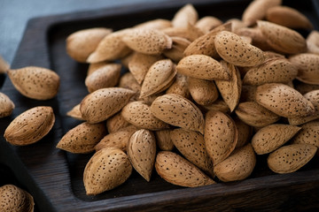 Close-up of unpeeled almond nuts on a black wooden serving tray, selective focus