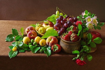 A variety of fruits and flowers on a table with a brown tablecloth.