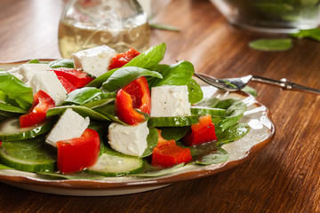 Fresh spinach salad with feta, cucumber and red paprika on a plate.